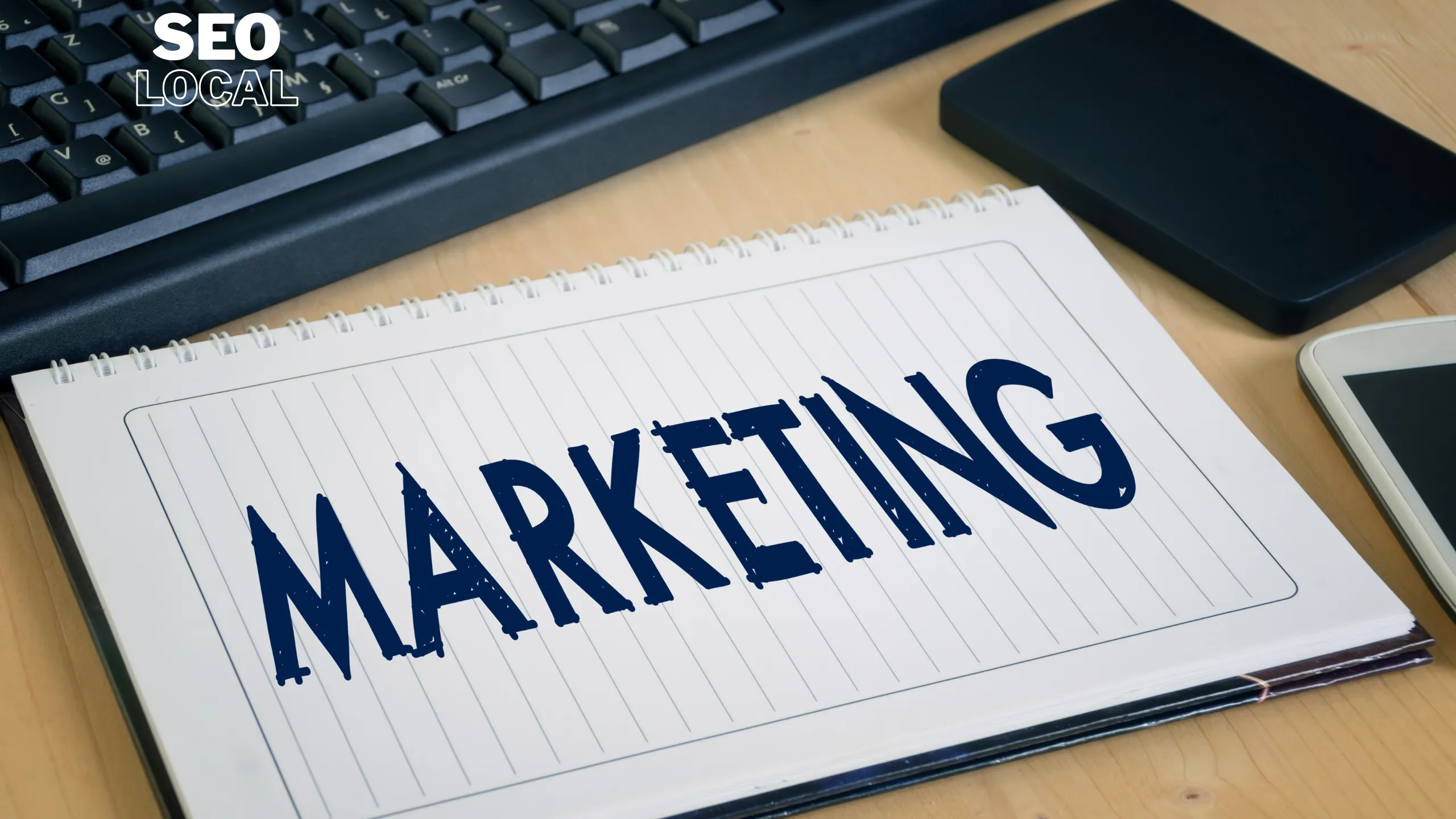 Un cuaderno con la palabra marketing sobre un escritorio, junto a un teclado y notas, durante la planificación de un presupuesto