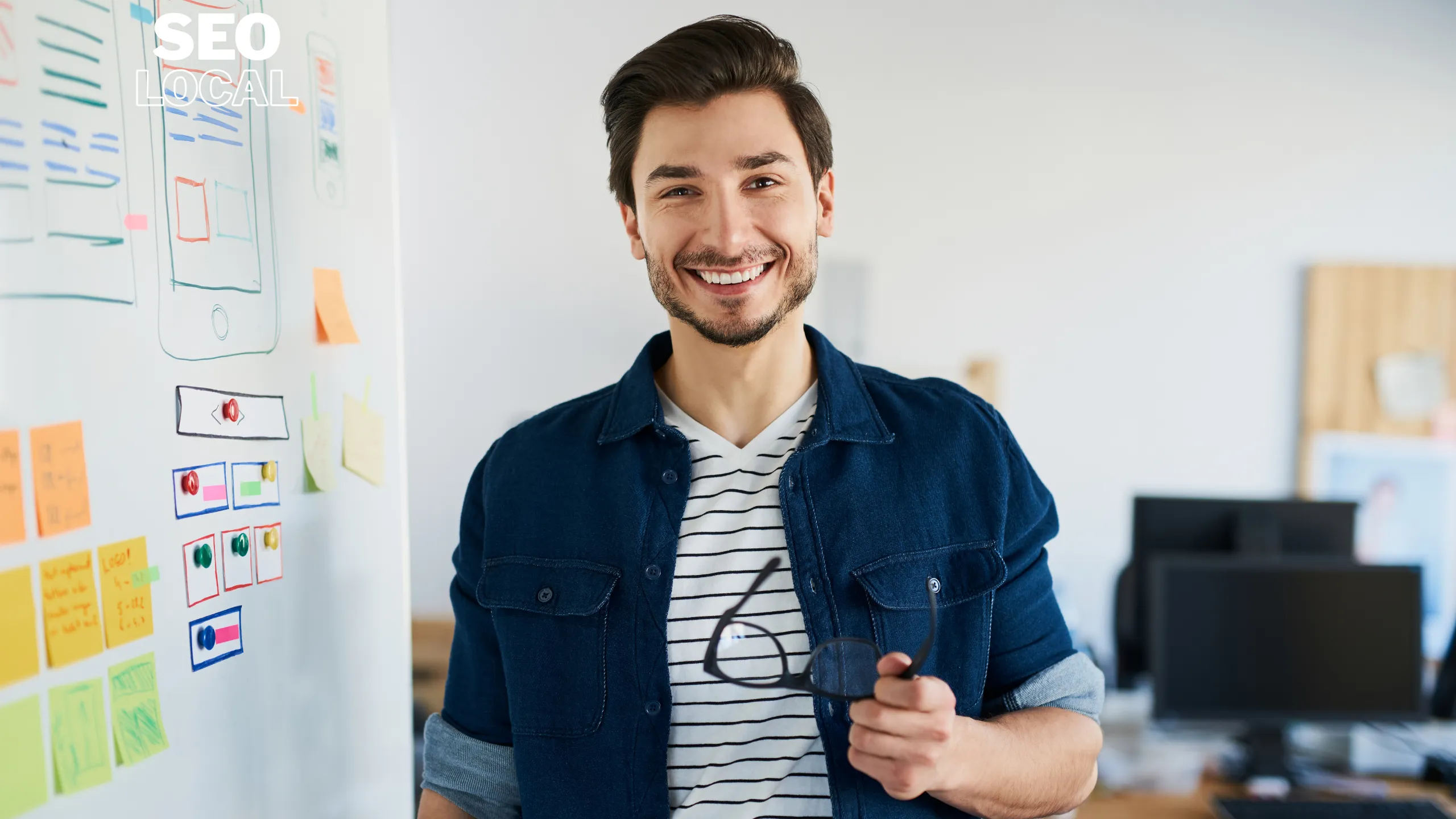 Un hombre sonriente frente a una pizarra con notas adhesivas, que representa al dueño de un negocio planificando su presencia local