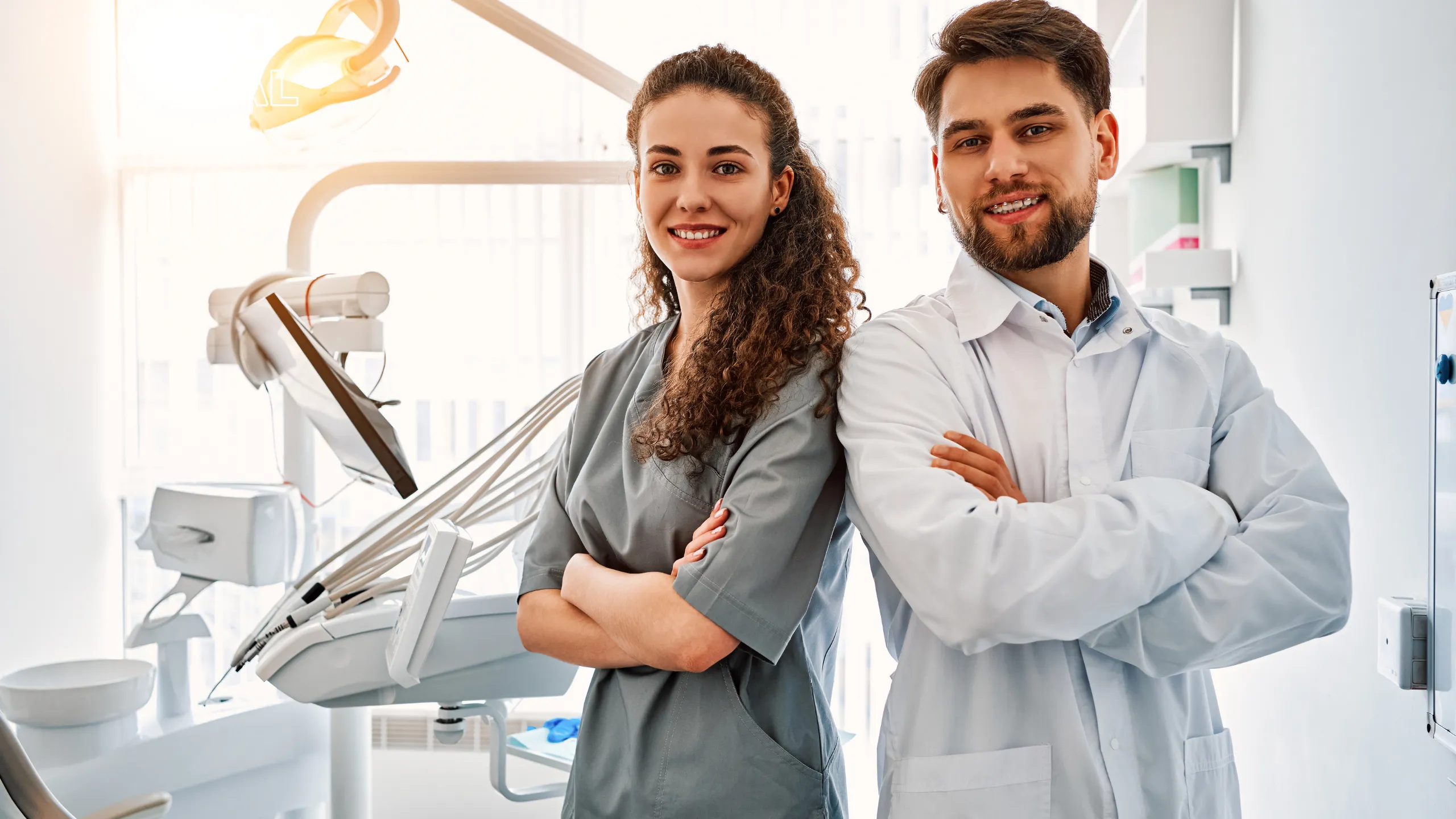 Una odontóloga y un odontólogo posan sonrientes junto a un sillón dental